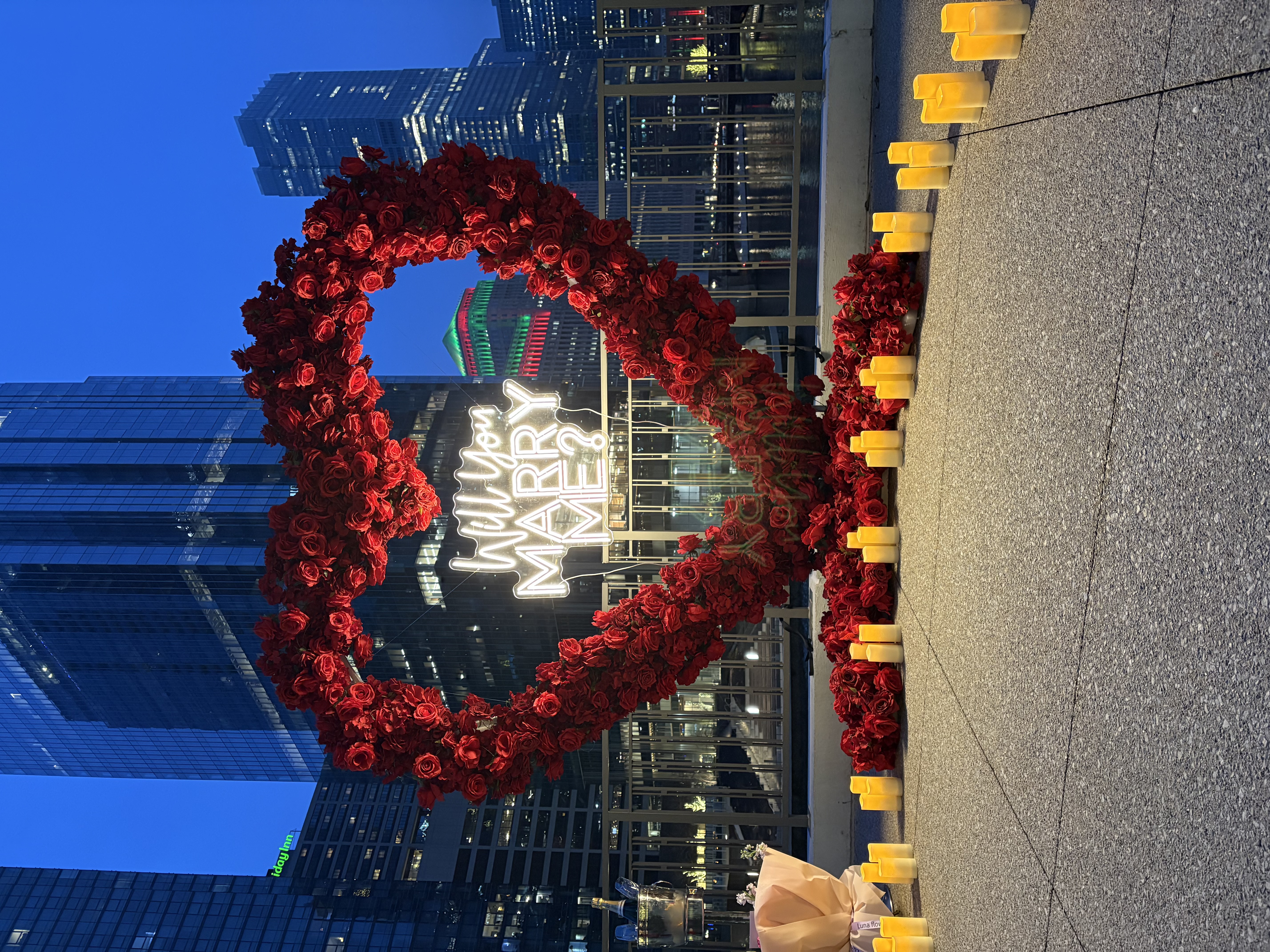 Chicago proposal planner setup — red floral heart arch rental with Will You Marry Me neon sign and red carpet