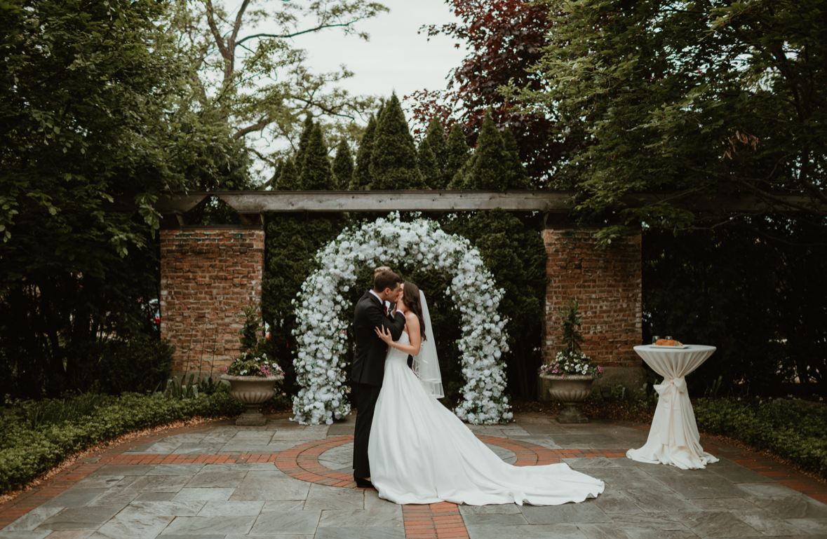 Wedding arch rental Chicago IL — bride and groom first kiss under white floral round arch outdoor ceremony | Chicago Flower Wall