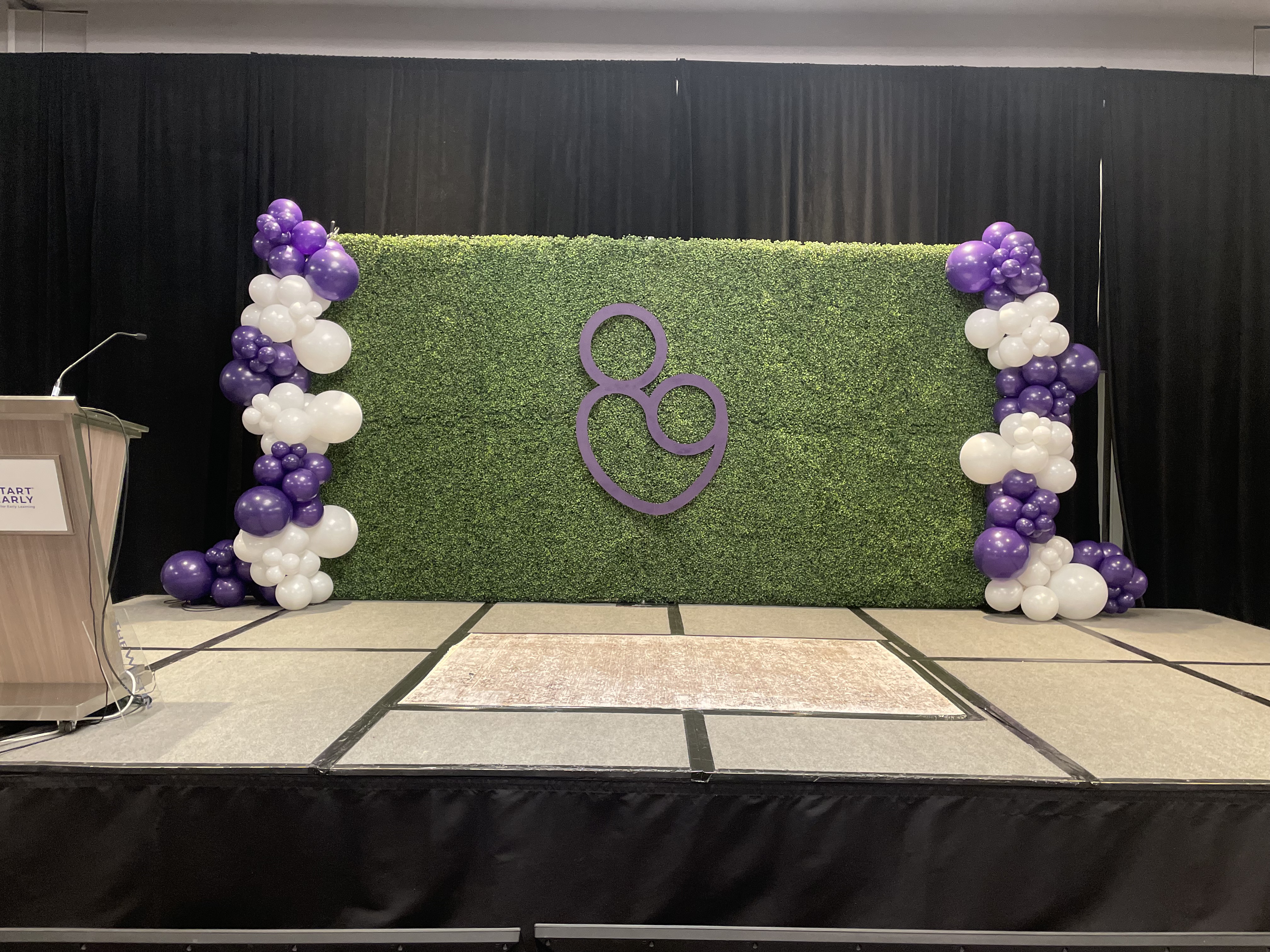 8x16 boxwood hedge wall rental Chicago corporate event stage backdrop with purple white balloon columns