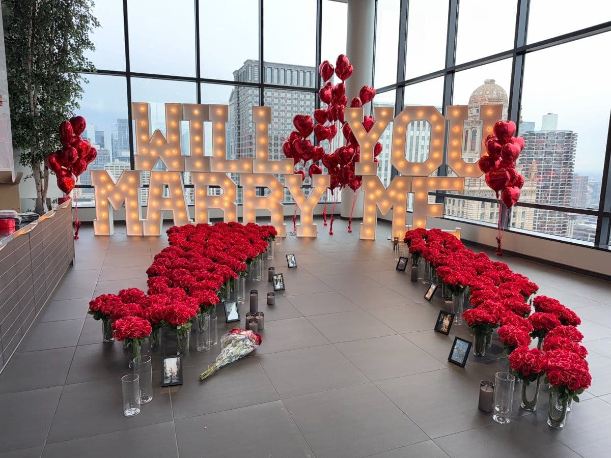 Chicago proposal decor — Will You Marry Me marquee letters with red roses heart balloons and Chicago skyline view