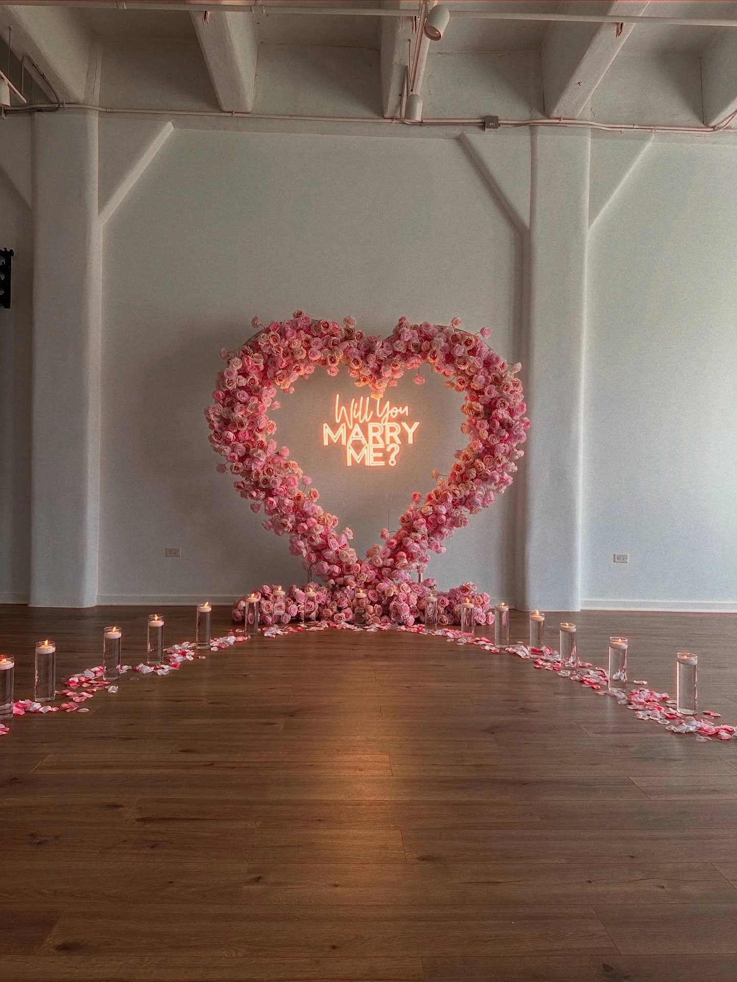 Heart arch rental in Chicago — pink rose heart arch with a Will You Marry Me neon sign, candles and petals on a wood floor