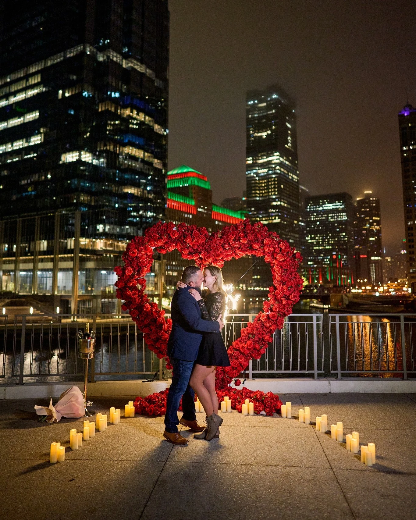 Heart shaped arch rental in Chicago with a couple embracing inside a candle heart outline in front of red roses and the Chicago skyline at night