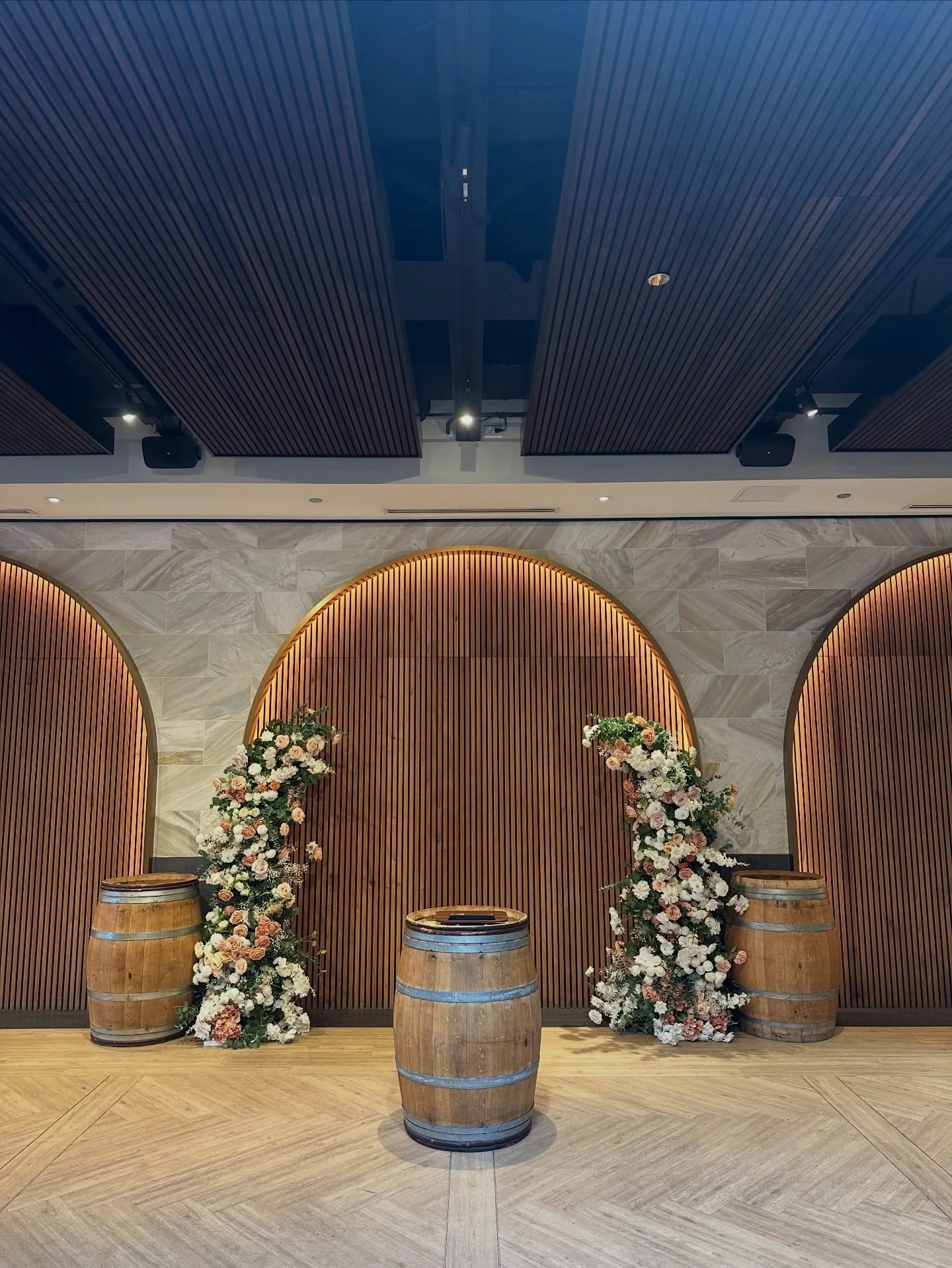 Wedding floral set rental in Chicago with two tall peach and cream ceremony floral pillars flanking wood-slat arches and wine barrels at Chicago Winery
