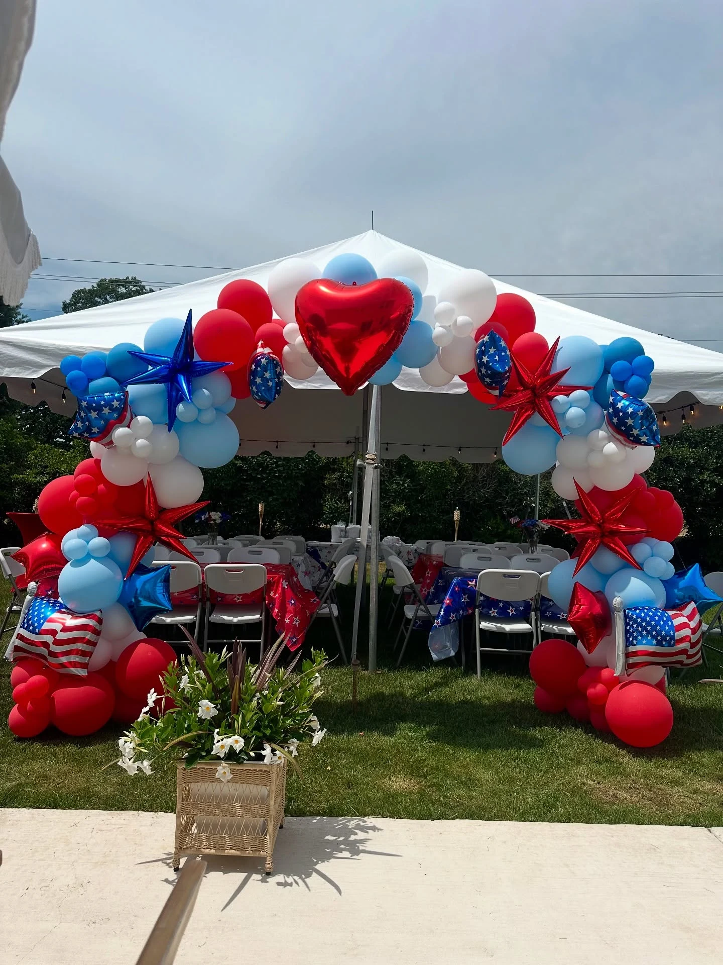 Fourth of July balloon arch rental in Chicago — a red white and blue organic balloon arch with a red heart foil at its crown and starburst and flag foils framing a white party tent entrance