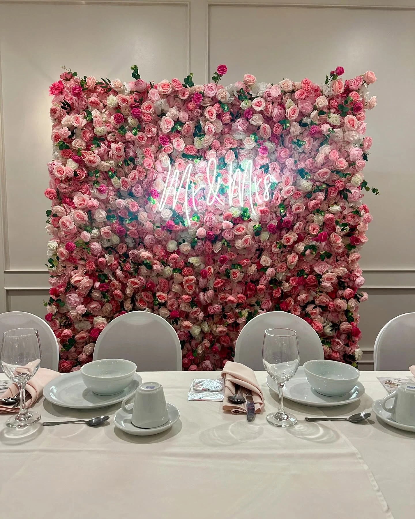 Flower wall rental in Chicago — pink rose flower wall with a white Mr & Mrs neon sign behind a wedding head table set with blush napkins