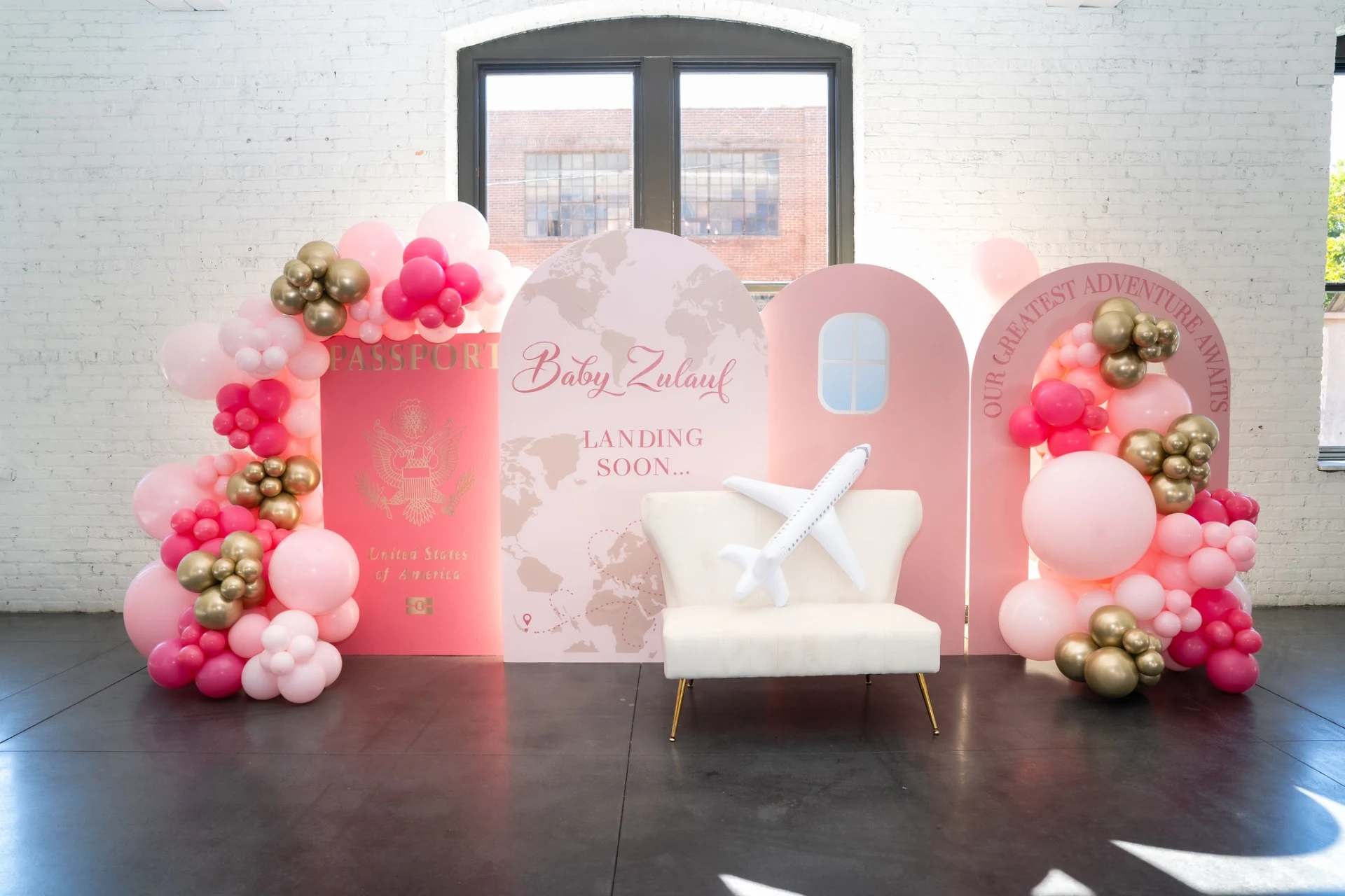 balloon arch rental in Chicago — pink and gold balloon garlands framing arched backdrop panels at a passport-themed baby shower in Aurora
