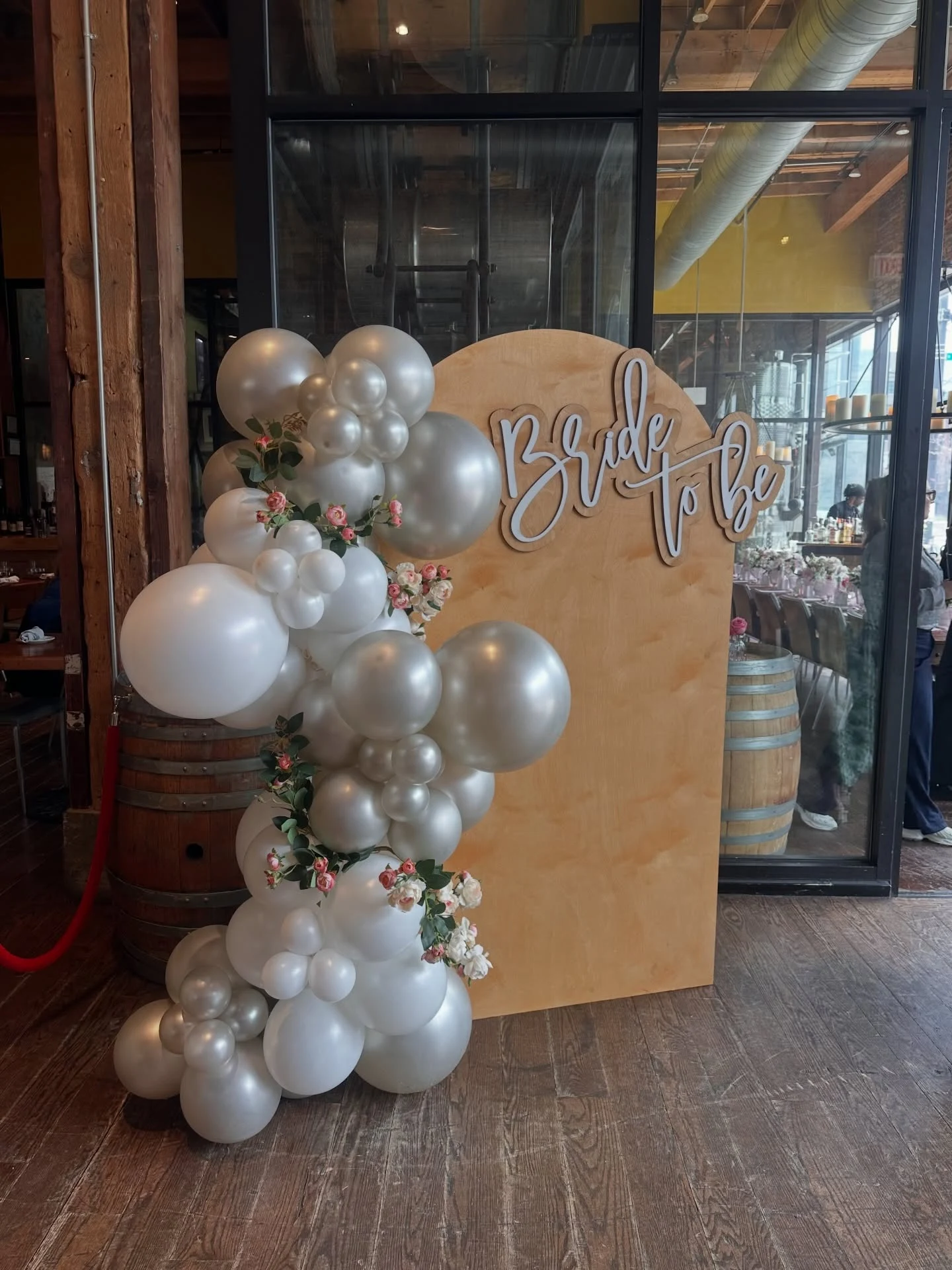 bridal shower backdrop rental in Chicago — natural wood arch panel with white Bride to Be script lettering and a pearl, silver and white balloon garland with rose sprigs at City Winery Chicago