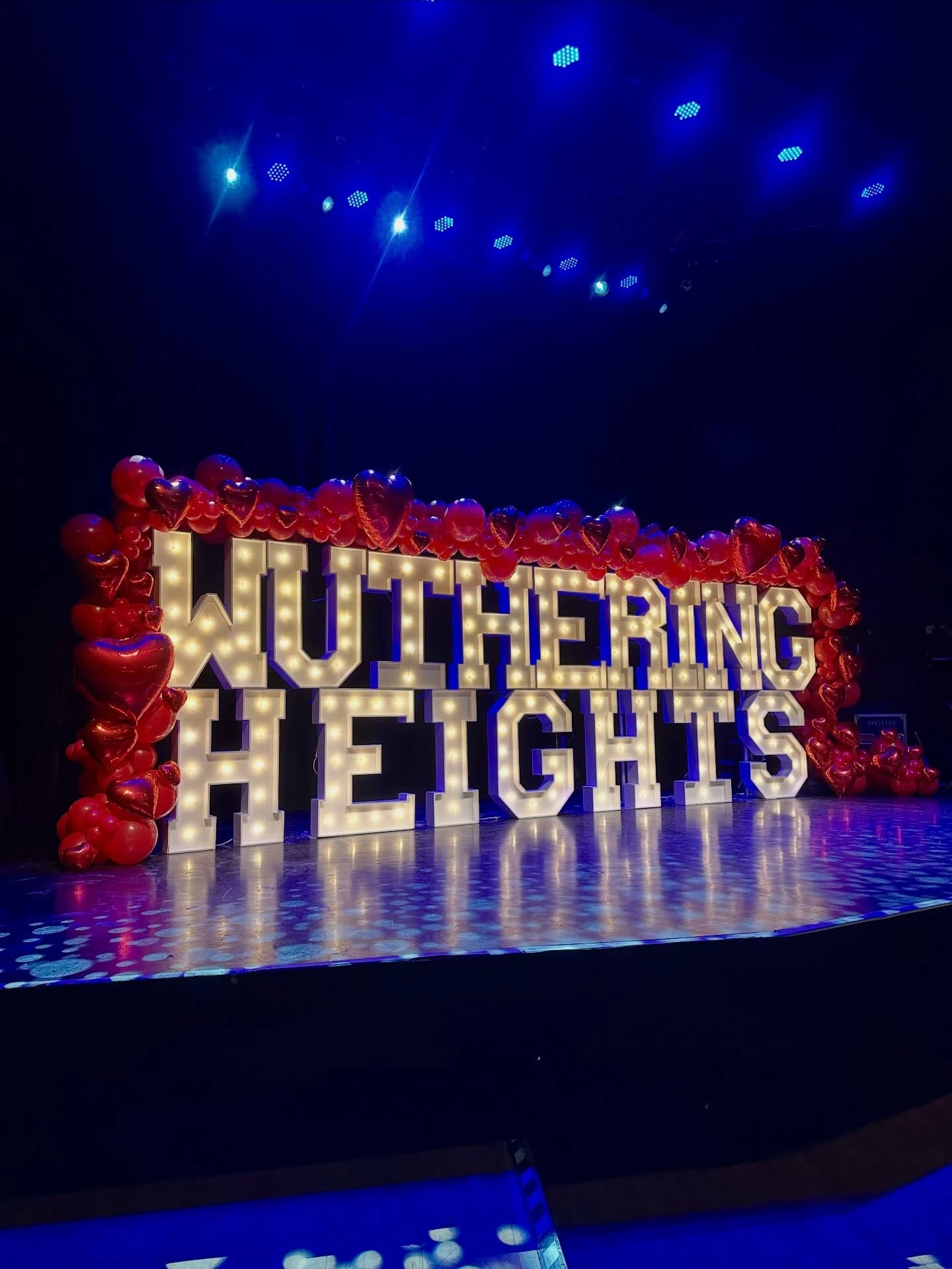 Light up marquee letters in Chicago spelling Wuthering Heights seen at an angle with blue stage lights and reflections on the glossy stage floor