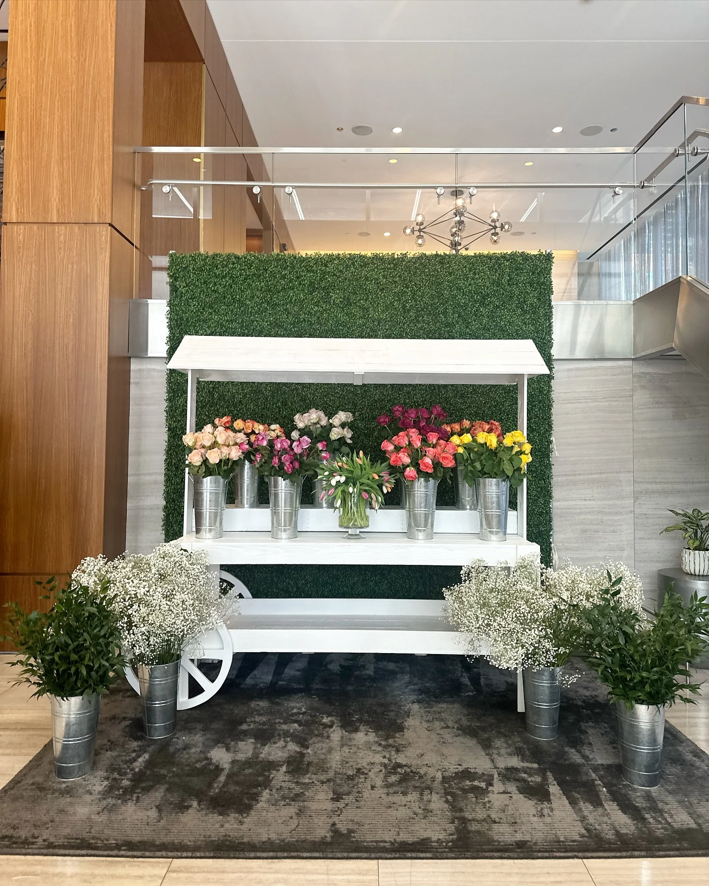 Flower cart rental in Chicago — white wooden Bloom Bar cart with buckets of roses in peach, pink, red and yellow in front of a green hedge wall at North Water Apartments