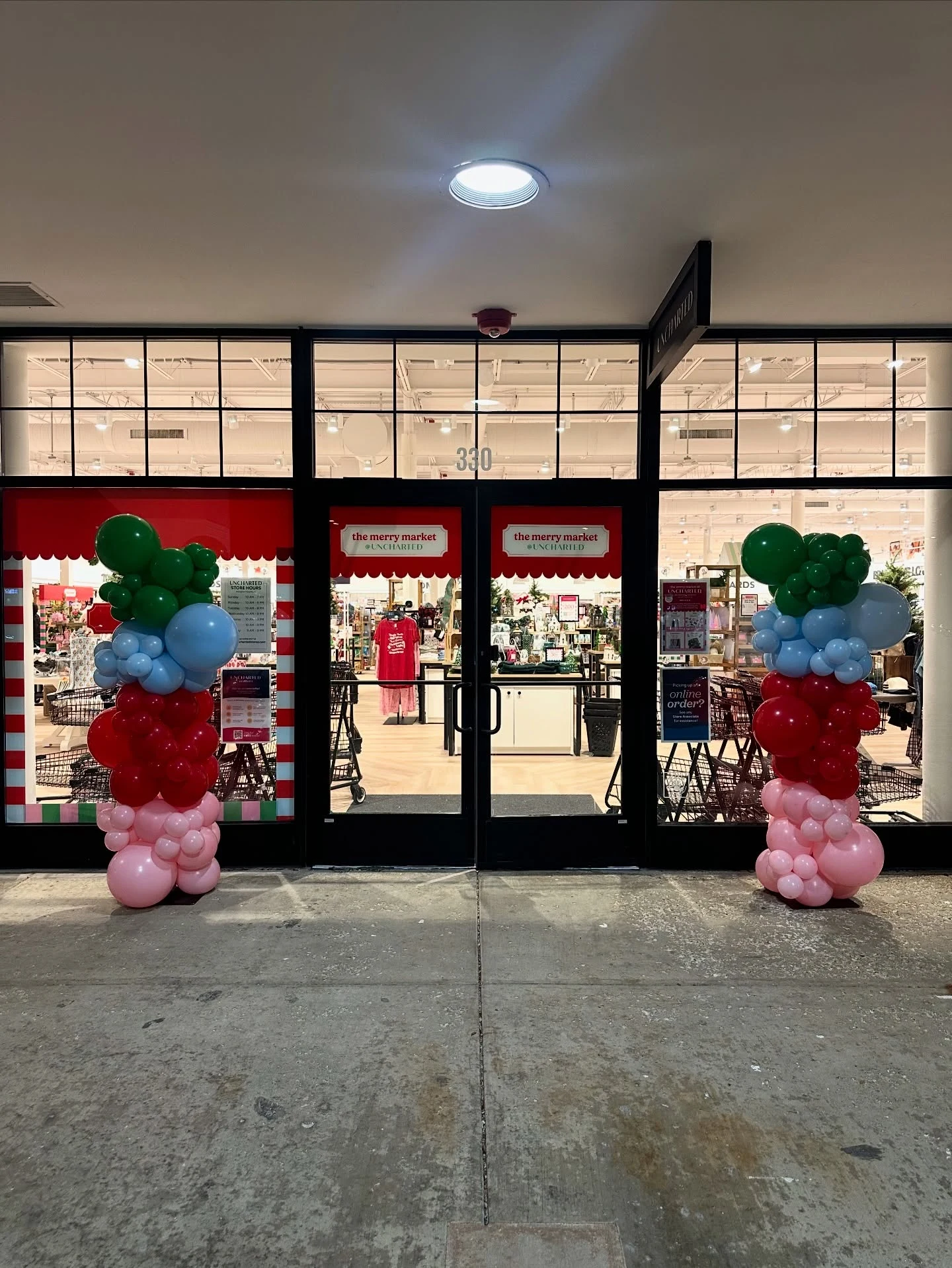 holiday balloon columns rental in Arlington Heights — two organic balloon columns in pink, red, light blue and green bands flanking the Merry Market entrance at Uncharted