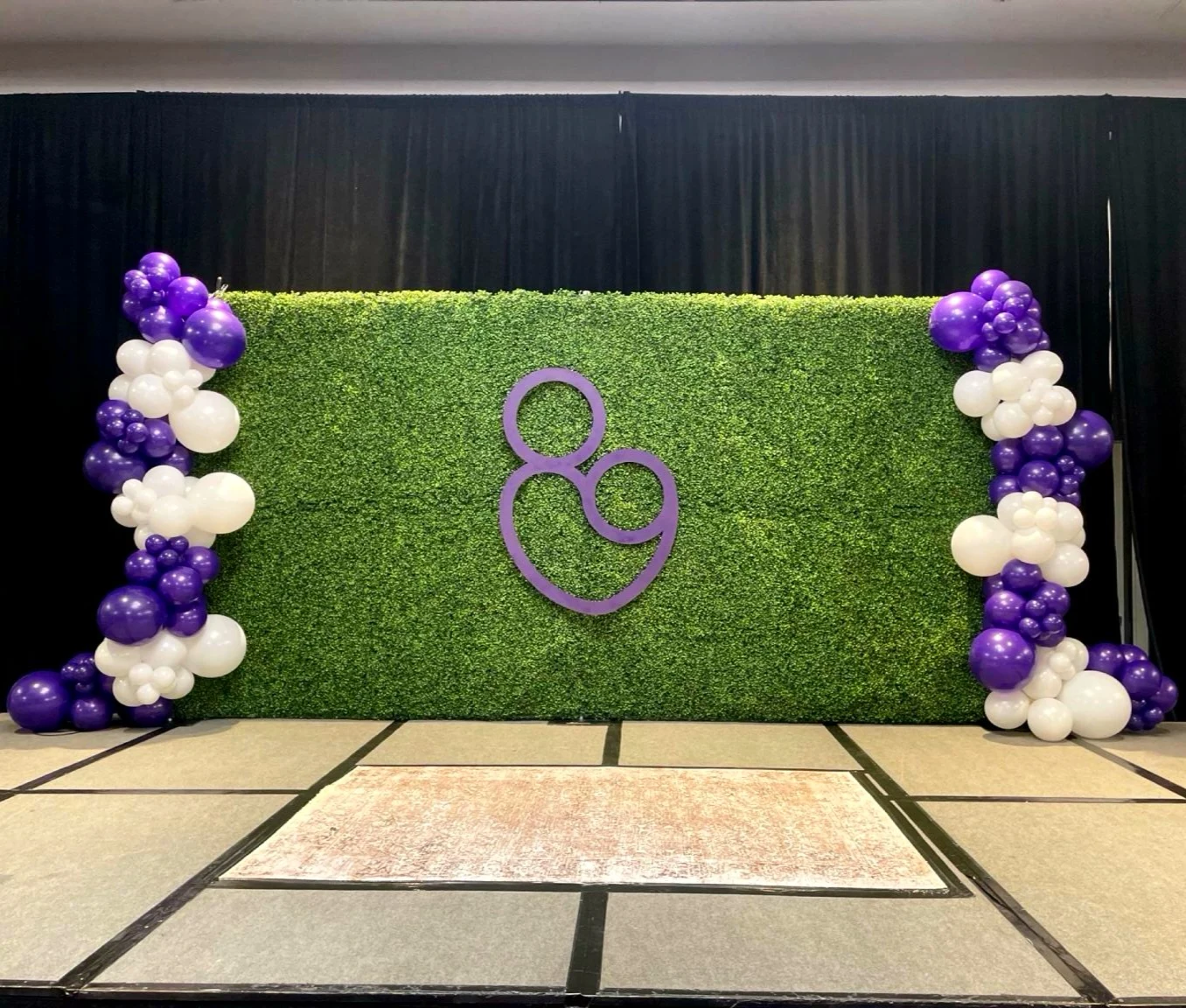 Hedge wall rental in Chicago with an 8x16 boxwood greenery wall, purple custom signage, and purple and white balloon garlands at a corporate event.