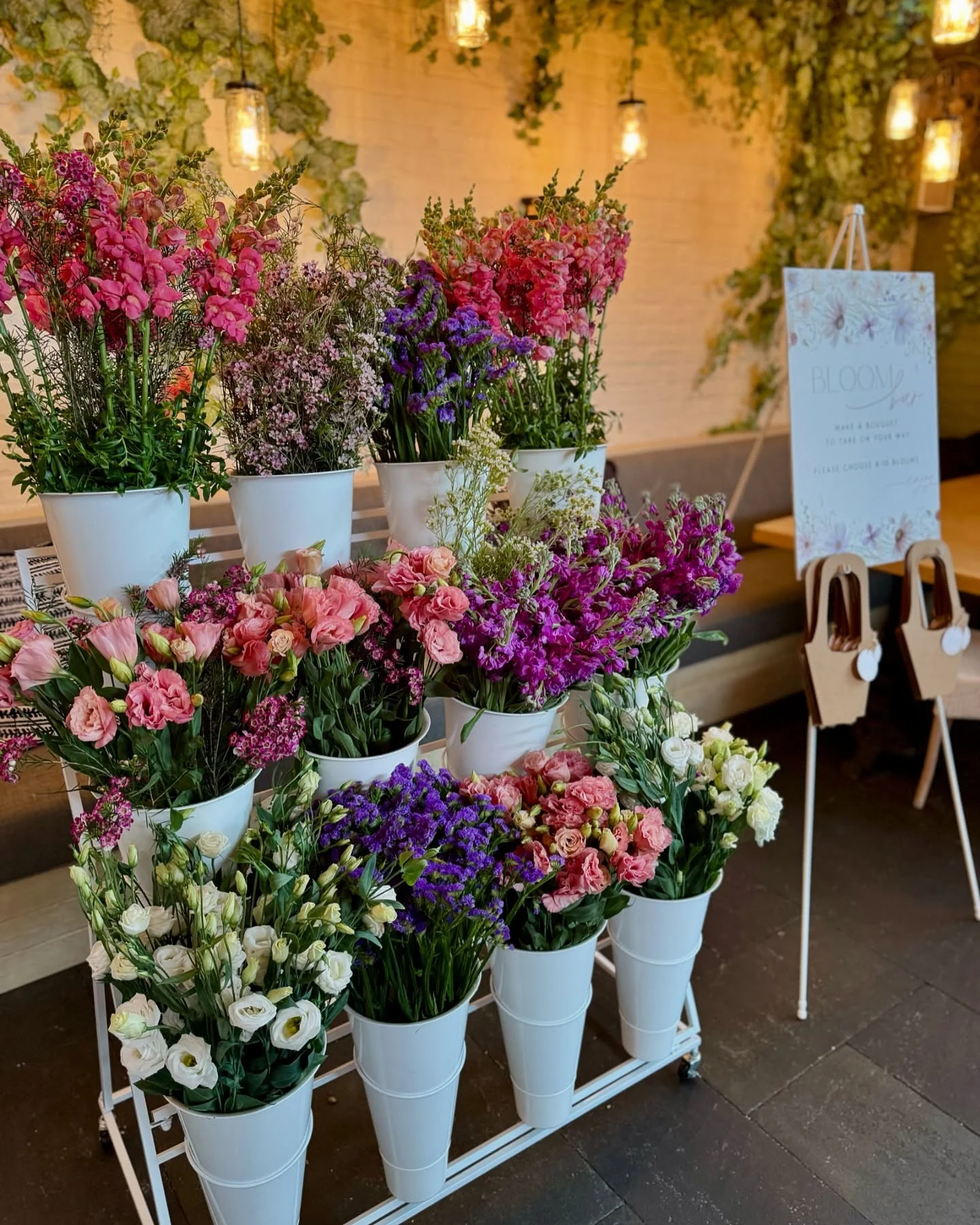 flower bar rental in Chicago — white multi-tiered Bloom Stand cart with buckets of fresh-cut snapdragons, statice and lisianthus and a 'make a bouquet' sign