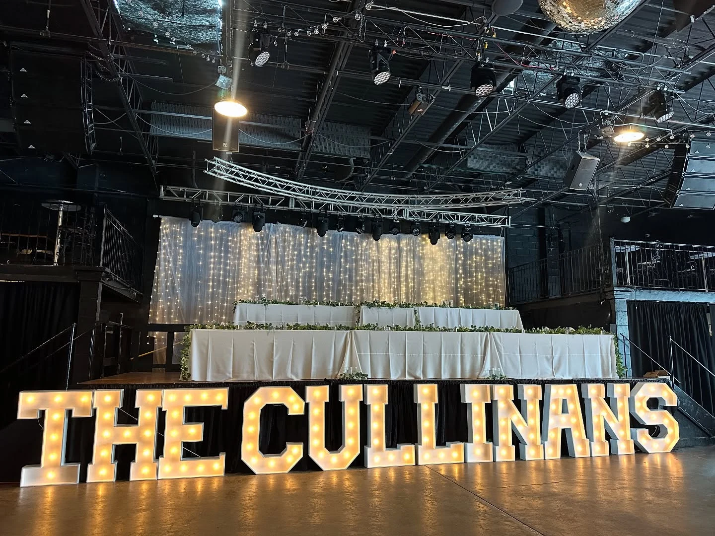 Marquee letter rental in Chicago — giant warm-bulb white marquee letters spelling THE CULLINANS on a dance floor in front of a raised head table with a fairy-light curtain in a dark industrial venue