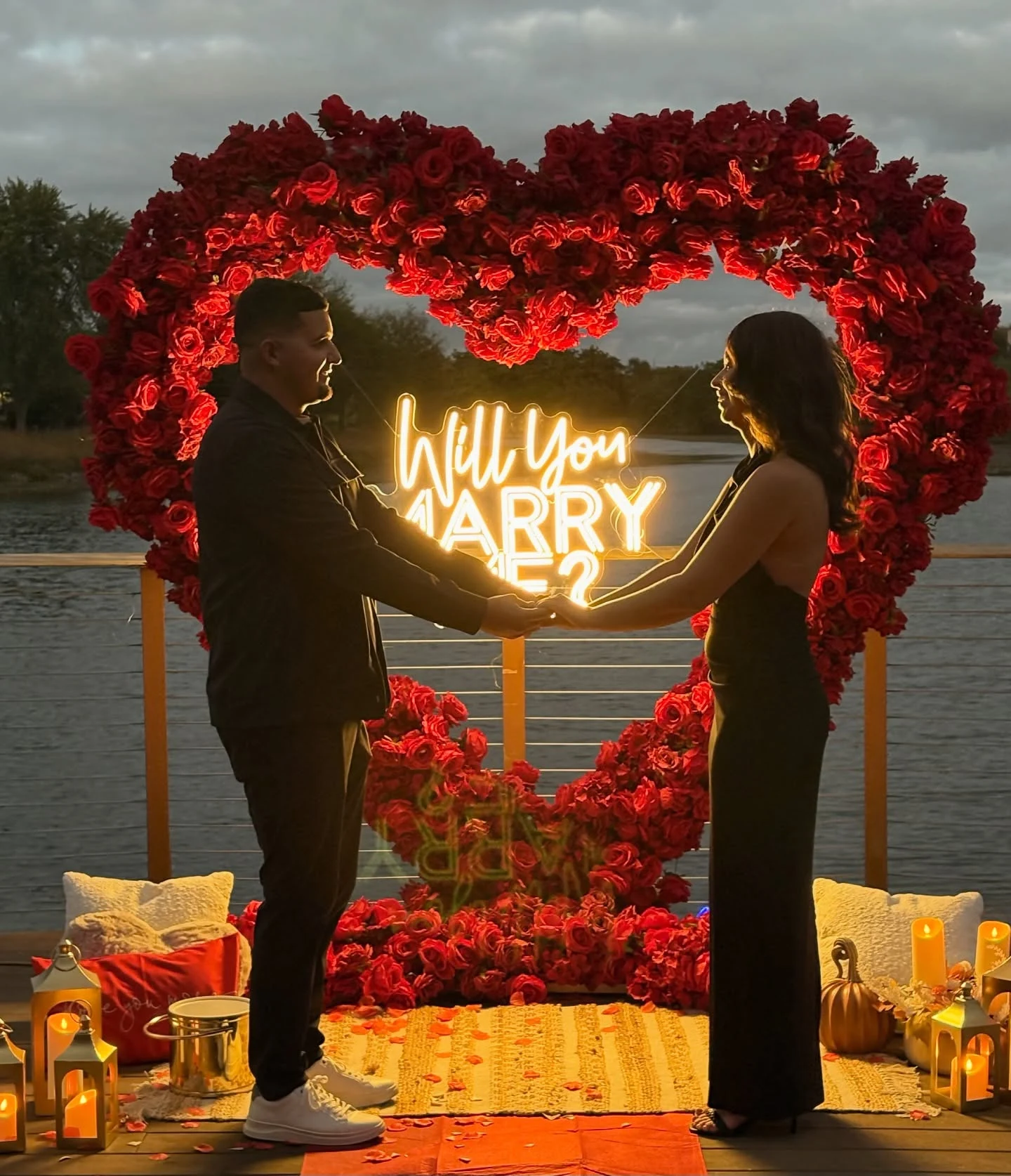 Red rose heart arch rental in Aurora at sunset with a couple holding hands inside the heart and a neon sign behind them