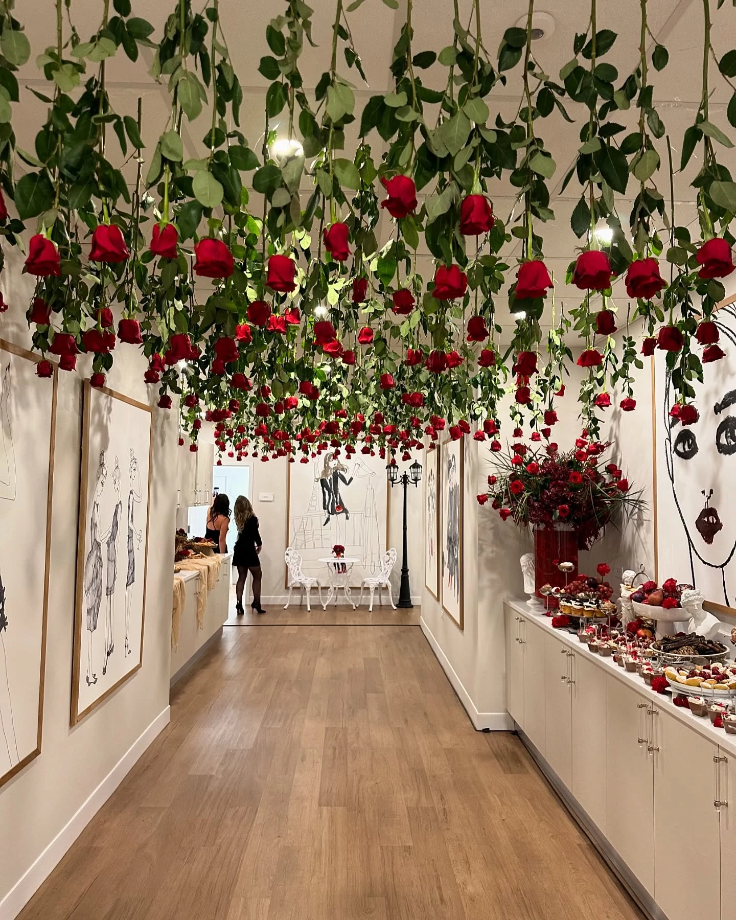 Hanging floral installation in Chicago — hundreds of red roses suspended upside-down from the ceiling over a wood-floor party room with Parisian fashion sketches