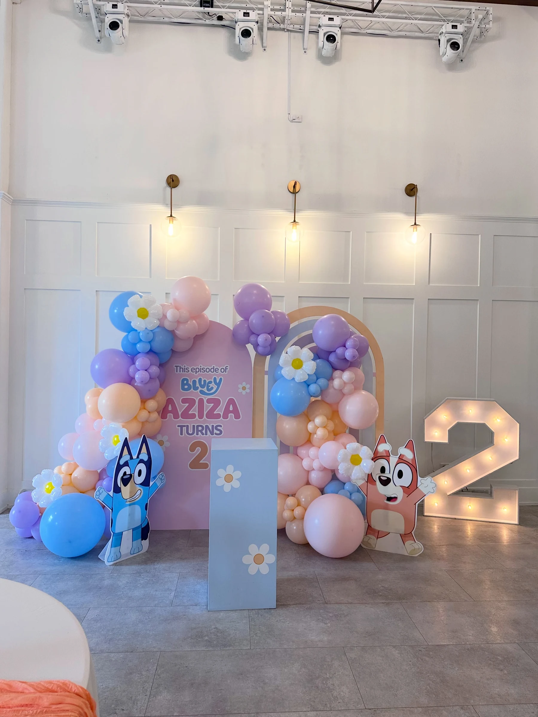 Bluey birthday backdrop rental in St. Charles — pink lettered name panel reading Aziza Turns 2, rainbow arch frame, pastel balloon garlands with daisy balloons, Bluey and Bingo cutouts and a light-up marquee number 2 at Cedar Fox Weddings