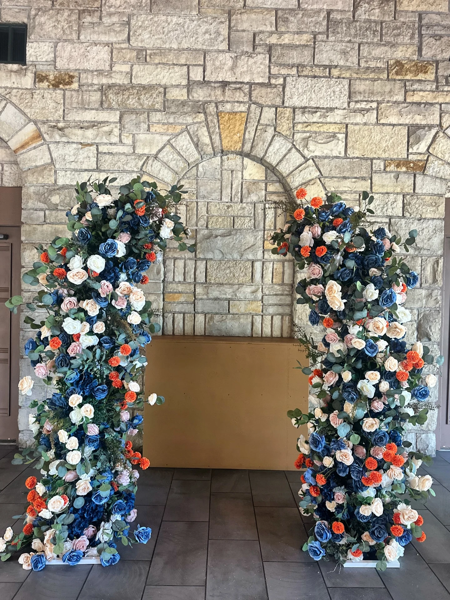 Floral pillar rental in Chicago — pair of tall pillars in navy blue roses, blush and ivory blooms, and burnt-orange accents with eucalyptus, standing against a stone wall