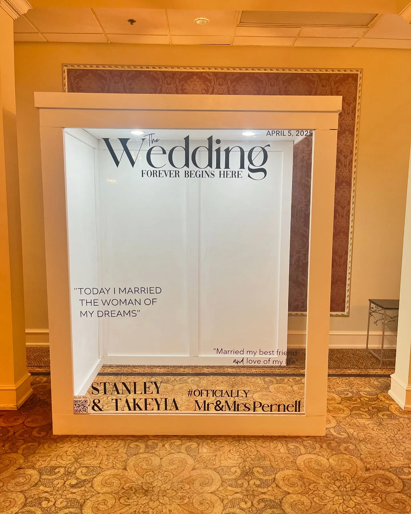 Magazine photo booth rental in Chicago — white magazine cover photo booth printed The Wedding, Forever Begins Here, for an April 5 2025 wedding, standing empty on a patterned ballroom carpet