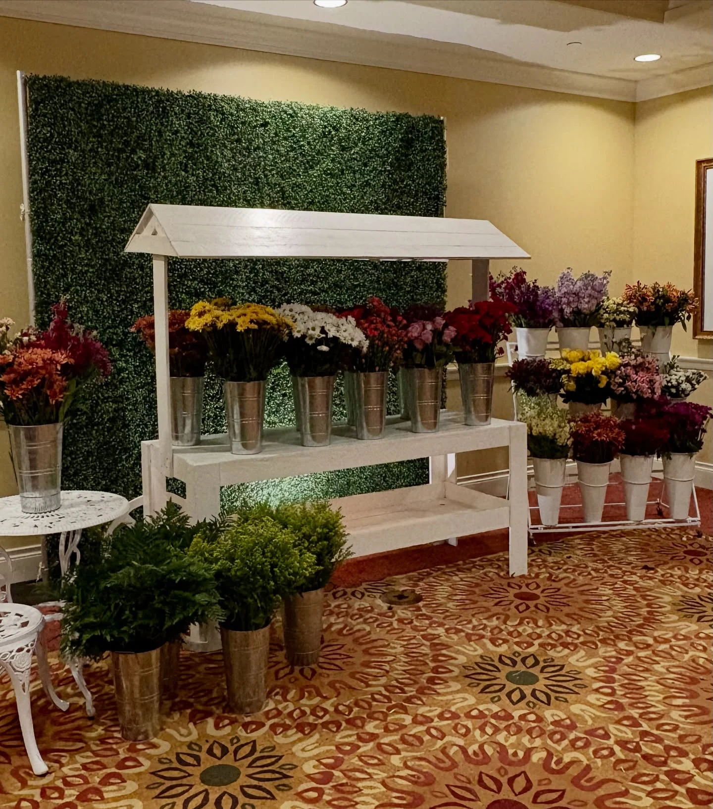 Flower cart rental in Chicago with a white canopy cart full of fresh flower buckets in yellow white red and pink in front of a boxwood hedge wall at a gala