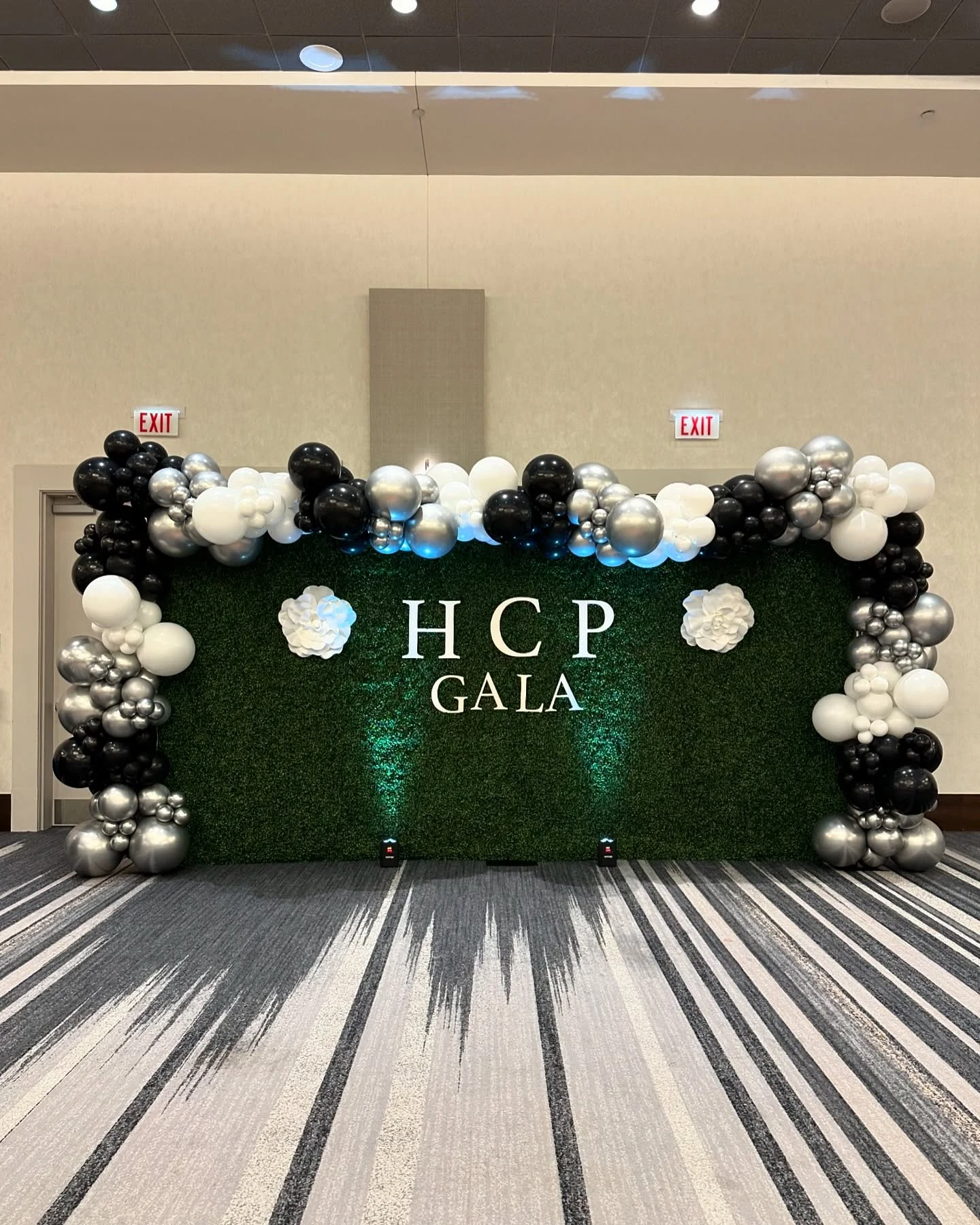 Boxwood hedge wall rental in Chicago — green hedge wall with HCP GALA wooden letters, white paper flowers and a black, white and silver balloon garland in a hotel ballroom